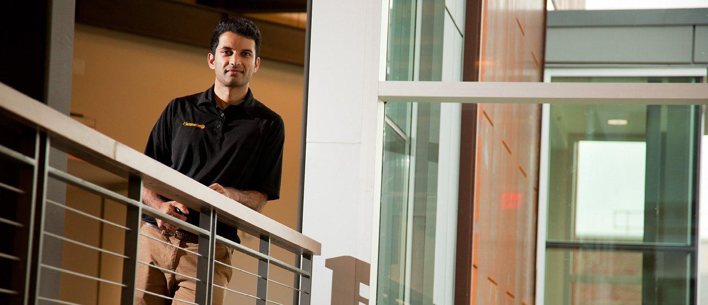 A man leaning on a railing in a hallway, looking down at the camera.